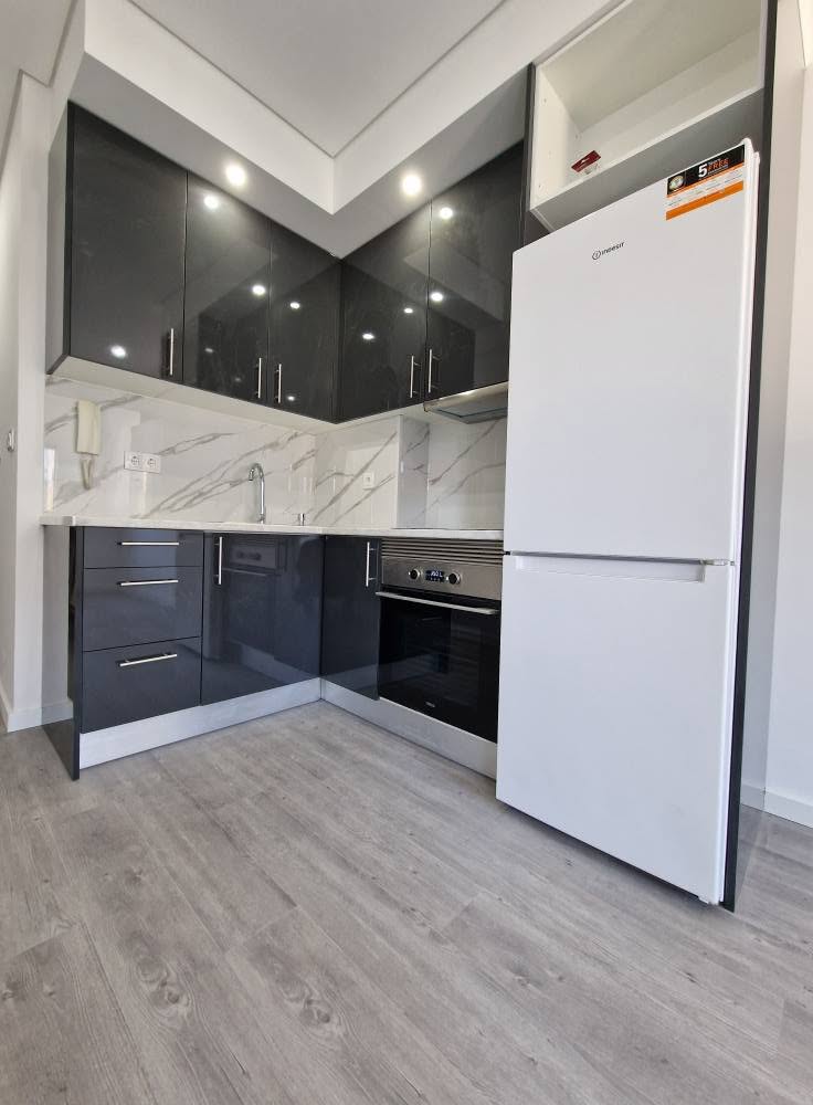 Cozinha concluída do apartamento T1, com armários em cinzento-escuro, bancada clara e eletrodomésticos instalados