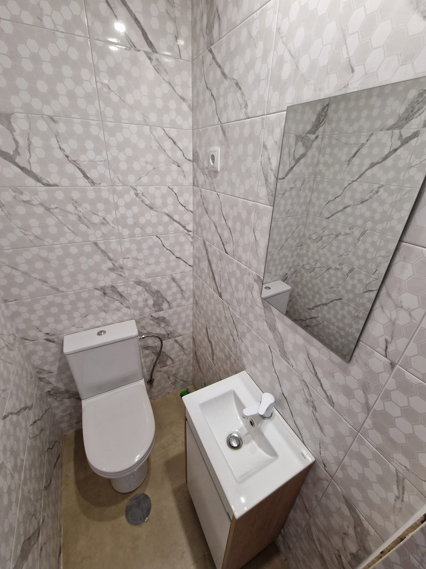 Casa de banho de serviço do apartamento T3 depois da remodelação, com sanita e móvel lavatório novos e revestimentos em efeito mármore